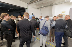 Uczestnicy szkolenia zgromadzeni wokół stanowiska obróbkowego w hali produkcyjnej, prowadzą rozmowy i obserwują prezentację ,